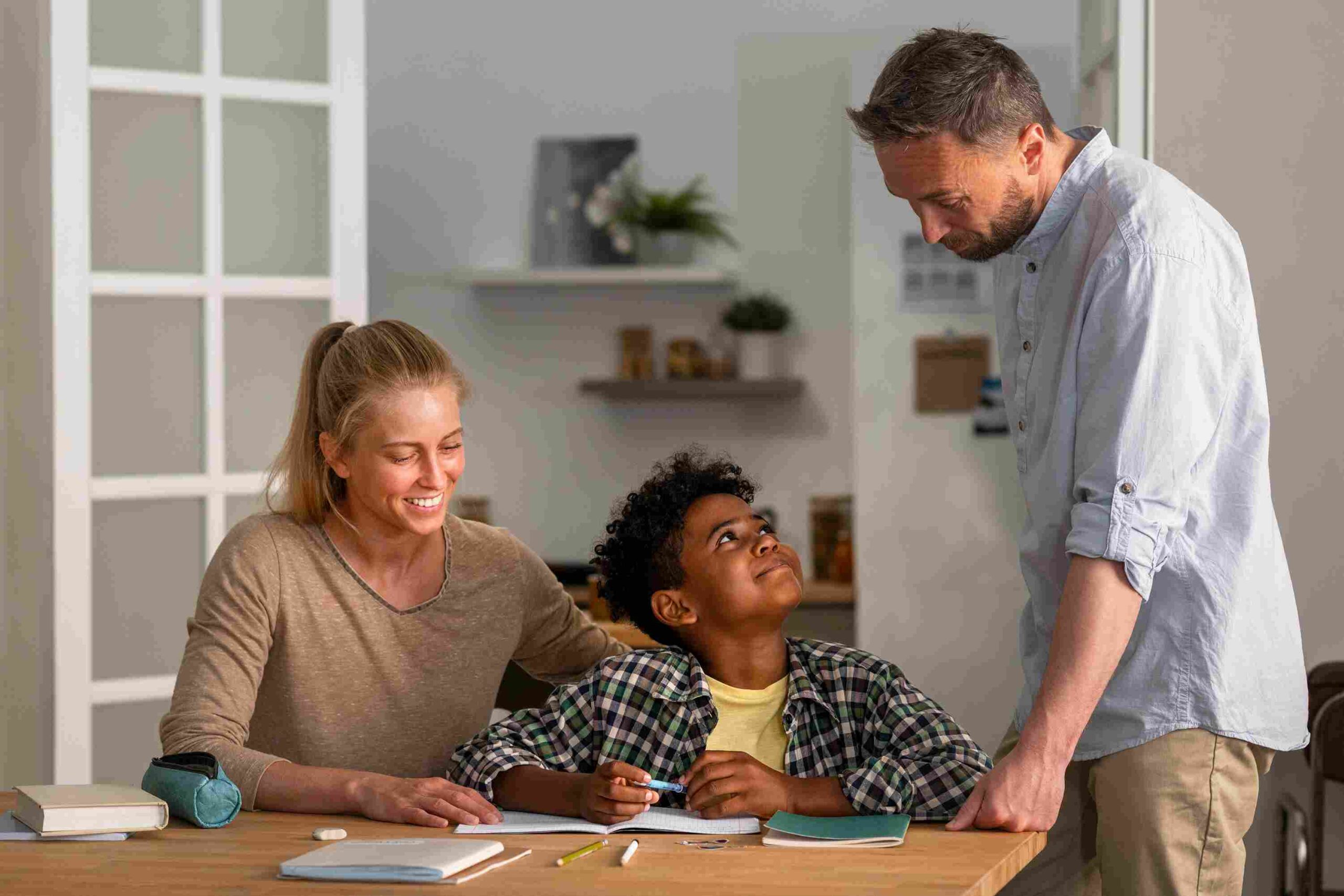 A boy doing homework with two adults smiling and helping him, representing supportive learning at Bexley Grammar Schools.